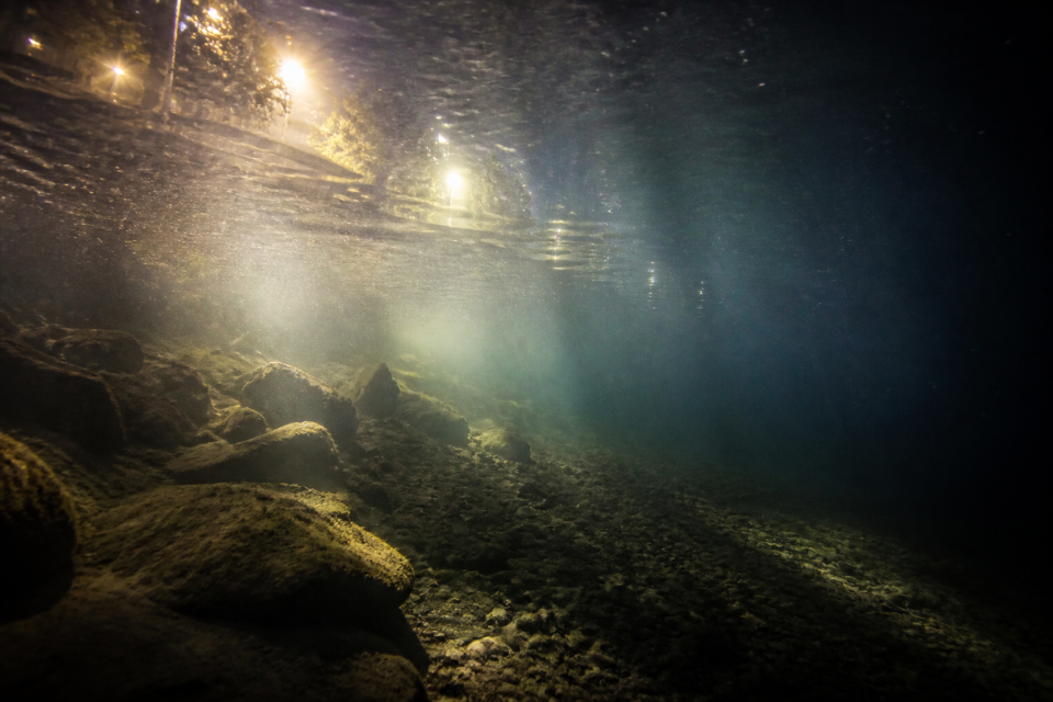 Lichtkegel im Flusswasser bei Nacht mit sichtbarer Streuung und Partikeln